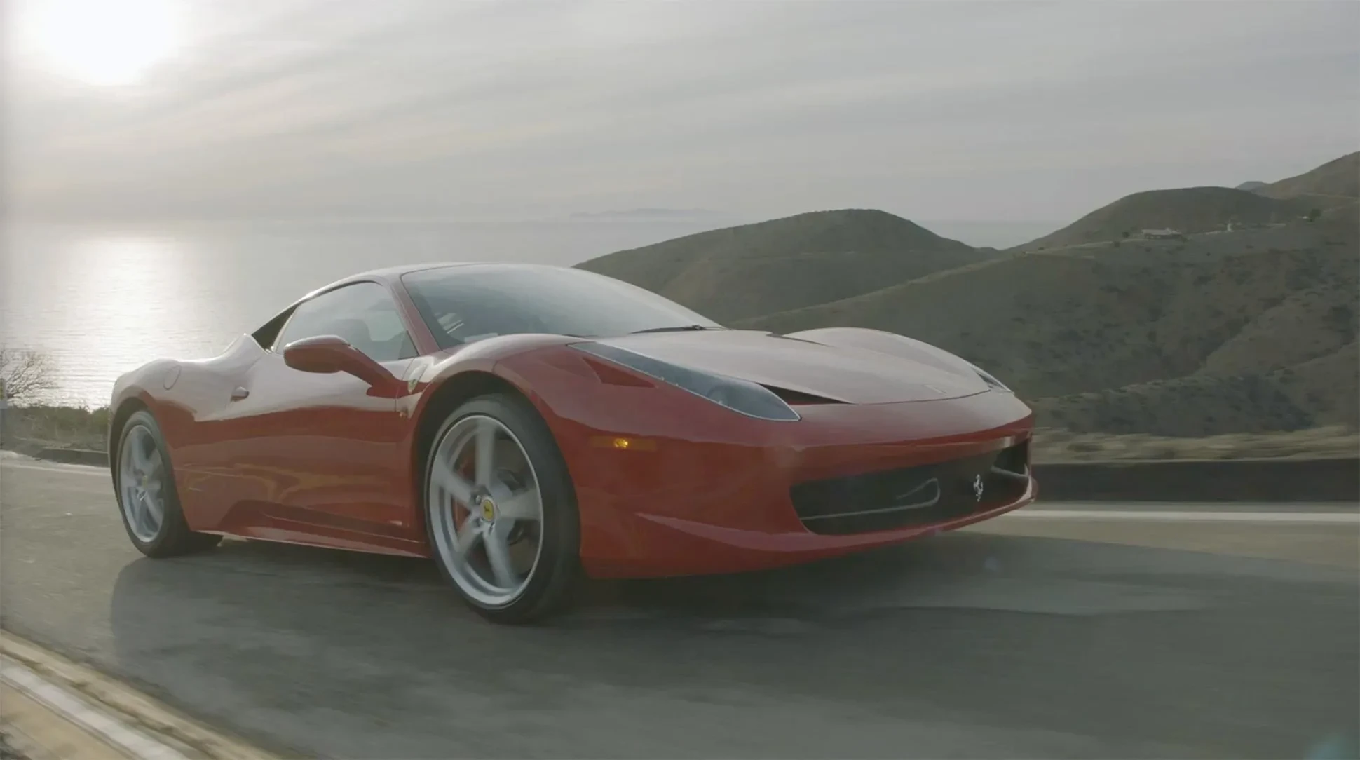 A red Ferrari driving on the coastline.